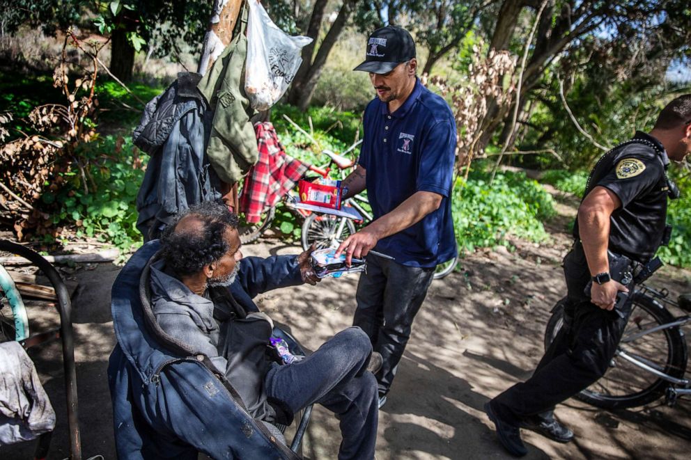 PHOTO: Anthony Aquiningos with the charity Alpha Project, provides some food and sanitation products to Norbert Alarcon, who sleeps in a tent in a wooded area of National City, Calif., March 4, 2020.