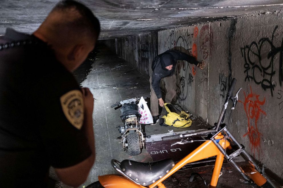 PHOTO: A police officer who is part of a homeless outreach unit talks with a man sheltering in a covered aqueduct in National City, Calif., March 4, 2020.