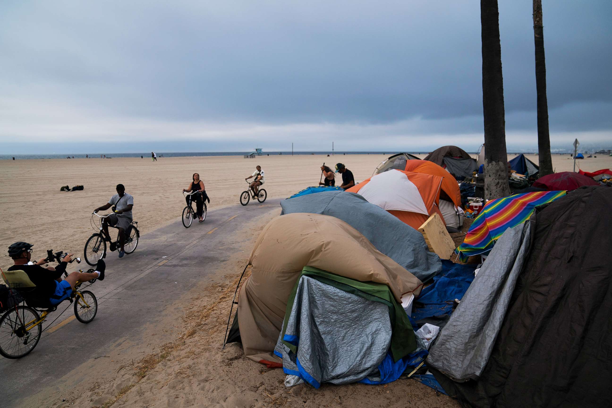 PHOTO: People ride their bikes past a homeless encampment set up along the boardwalk in the Venice neighborhood of Los Angeles on June 29, 2021.