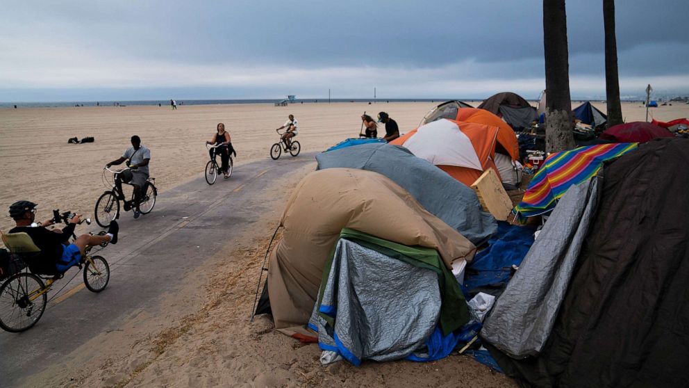 PHOTO: People ride their bikes past a homeless encampment set up along the boardwalk in the Venice neighborhood of Los Angeles on June 29, 2021.