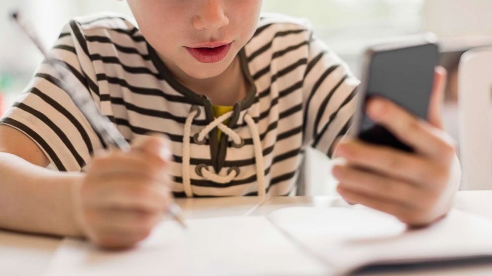 PHOTO: A stock photo depicts a young boy using a phone while doing his homework.