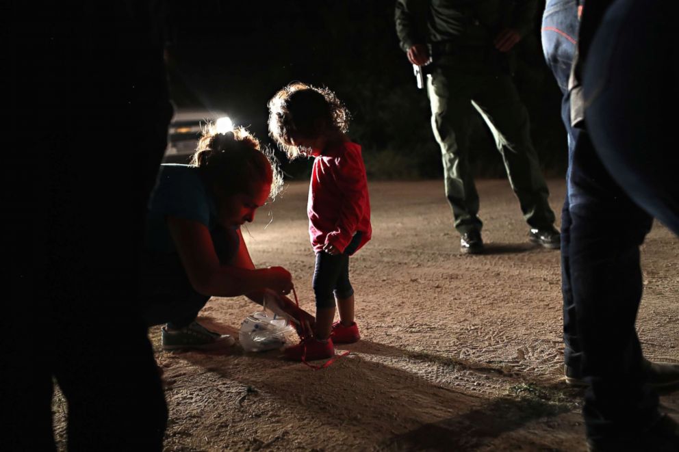 PHOTO: A Honduran mother removes her two-year-old daughter's shoe laces, as required by U.S. Border Patrol agents, after being detained near the U.S.-Mexico border on June 12, 2018, in McAllen, Texas. 