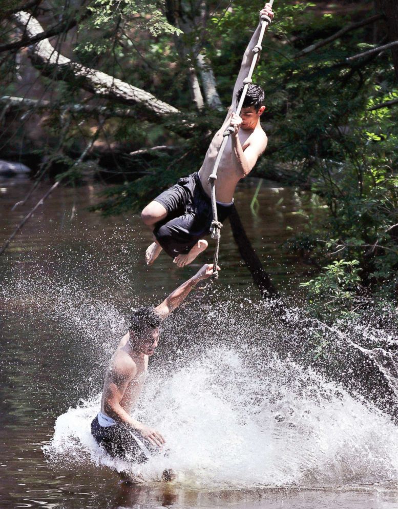 PHOTO: Two men splash into the Squannacook River on a rope swing while cooling off in Groton, Mass., July 2, 2018.