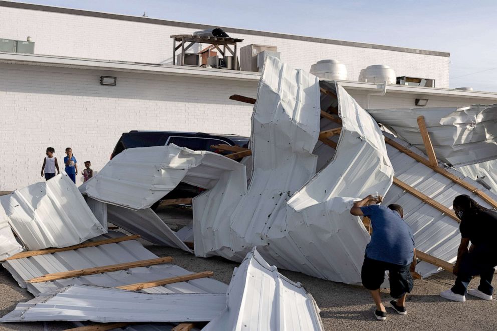 PHOTO: Siblings watch as men move the scaffolding that fell on top of a vehicle outside of a hotel in the aftermath of Hurricane Ida in Houma, La,  August 30, 2021.