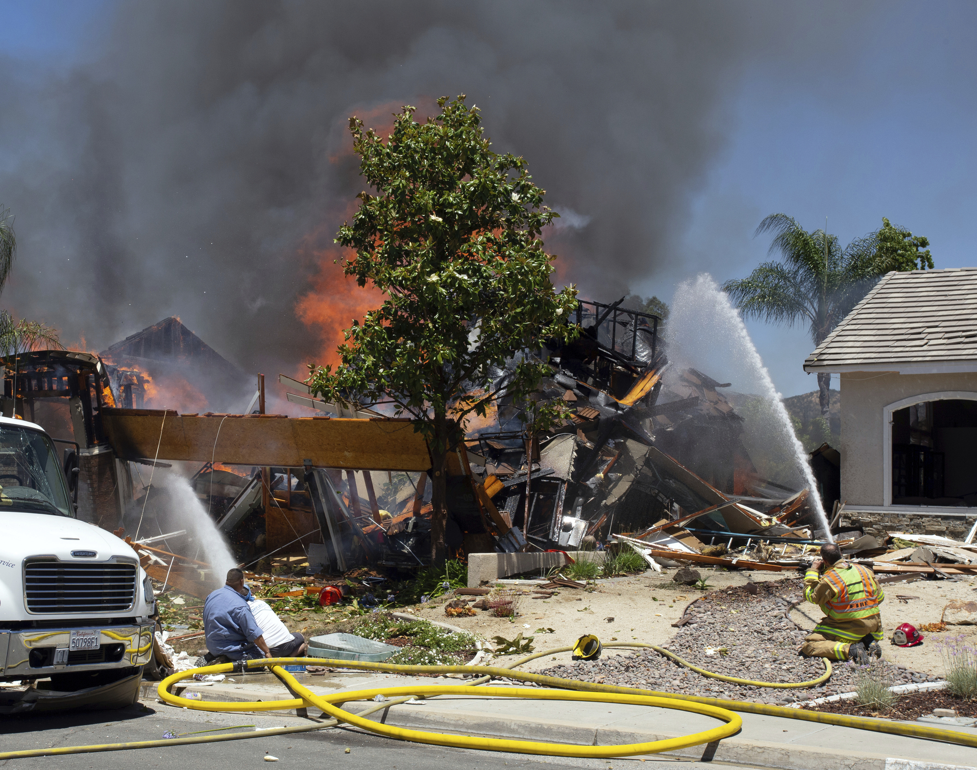 PHOTO: A firefighter and civilians train fire hoses on a burning home after an explosion and fire destroyed the home in Murrieta, Calif., sending up thick flames and closing several streets.