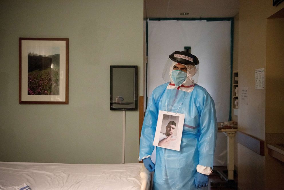 PHOTO: Fernando Olvera wears a picture around his neck for patients to know what he looks like while wearing personal protective equipment as he visits the room of a COVID-19 patient at United Memorial Medical Center in Houston, Texas, July 25, 2020.