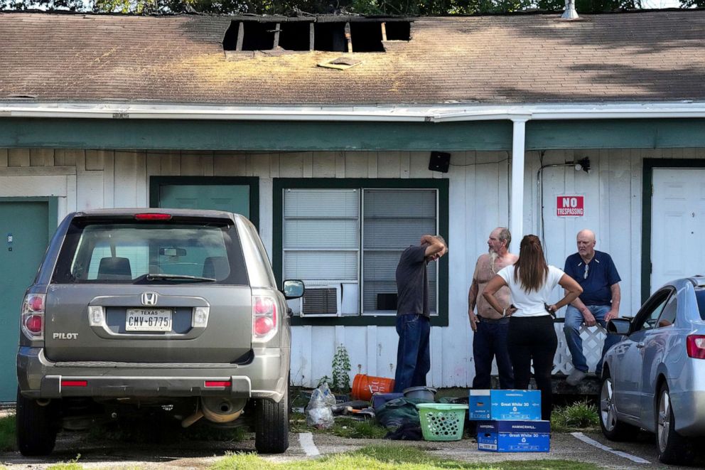 PHOTO: Neighbors stand around a multi-room renting facility in the aftermath of a fatal shooting in Houston, Aug. 28, 2022