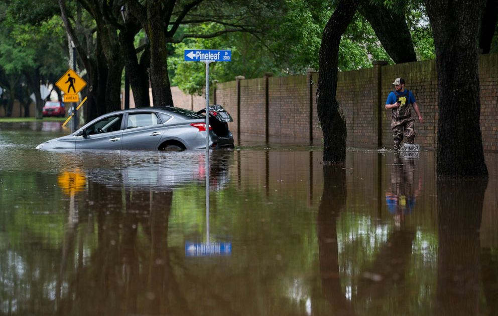PHOTO: A man walks past a flooded car on Williams Trace Boulevard in Sugar Land, Texas, on Wednesday, May 8, 2019.