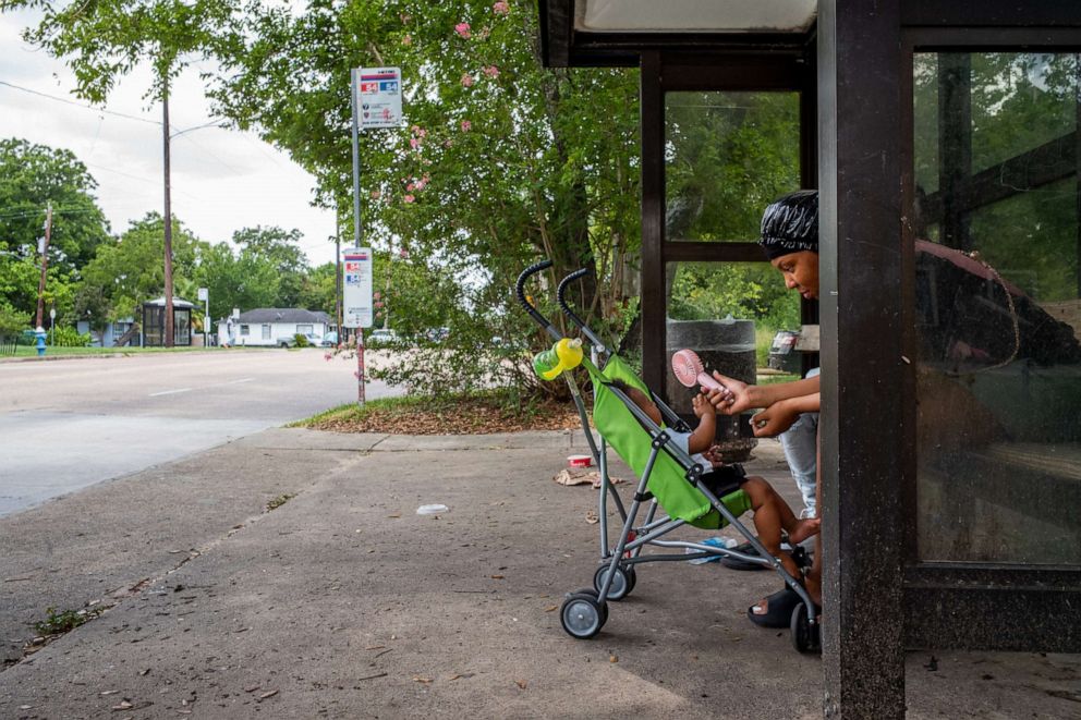 PHOTO: A mother cools her son with a portable fan while waiting for the bus during a heatwave in Houston, July 21, 2022.
