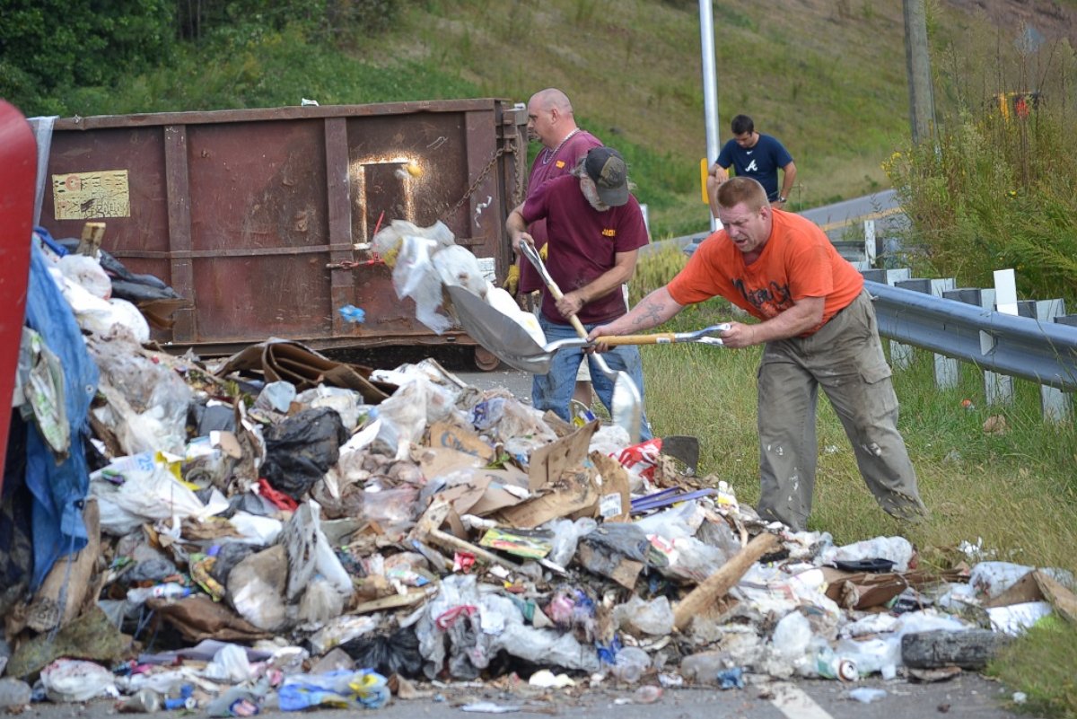PHOTO: Officials help clean up mounds of garbage after a garbage truck topples to its side enveloping a minivan.