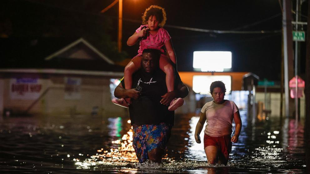 PHOTO: Jamir Lewis wades through flood waters with his two daughters Nylah and Aria due to storm surge from Hurricane Helene, Sept. 27, 2024 in Crystal River, Fla.