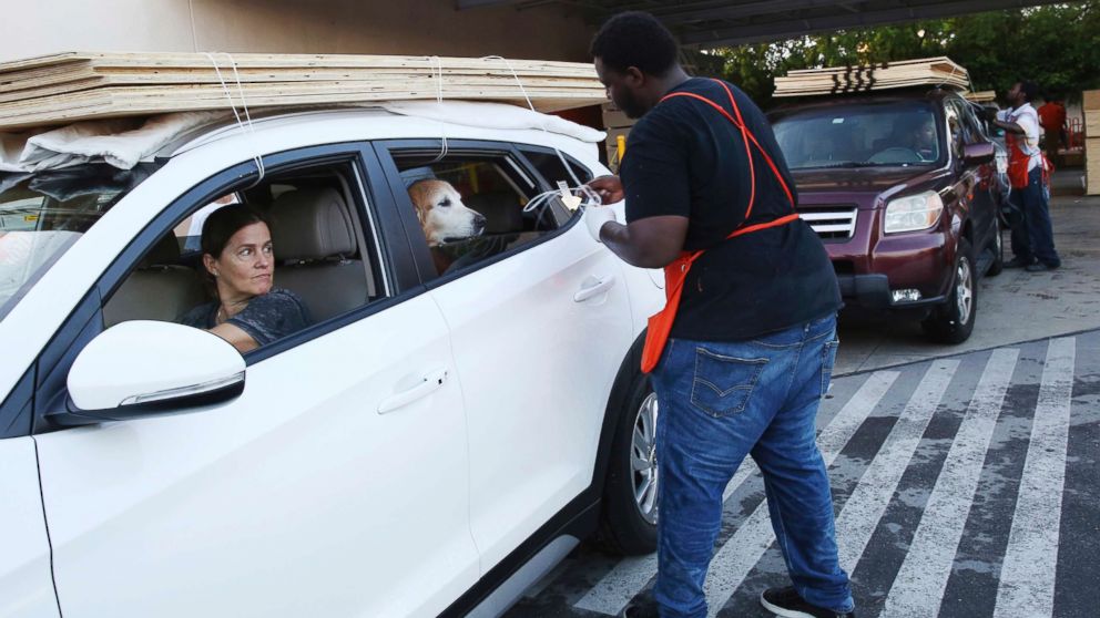 Beatriz Bustamante and her dog Simon wait as Qawrence Symonette secures sheets of plywood on her car at a store in North Miami, Sept. 6, 2017. 