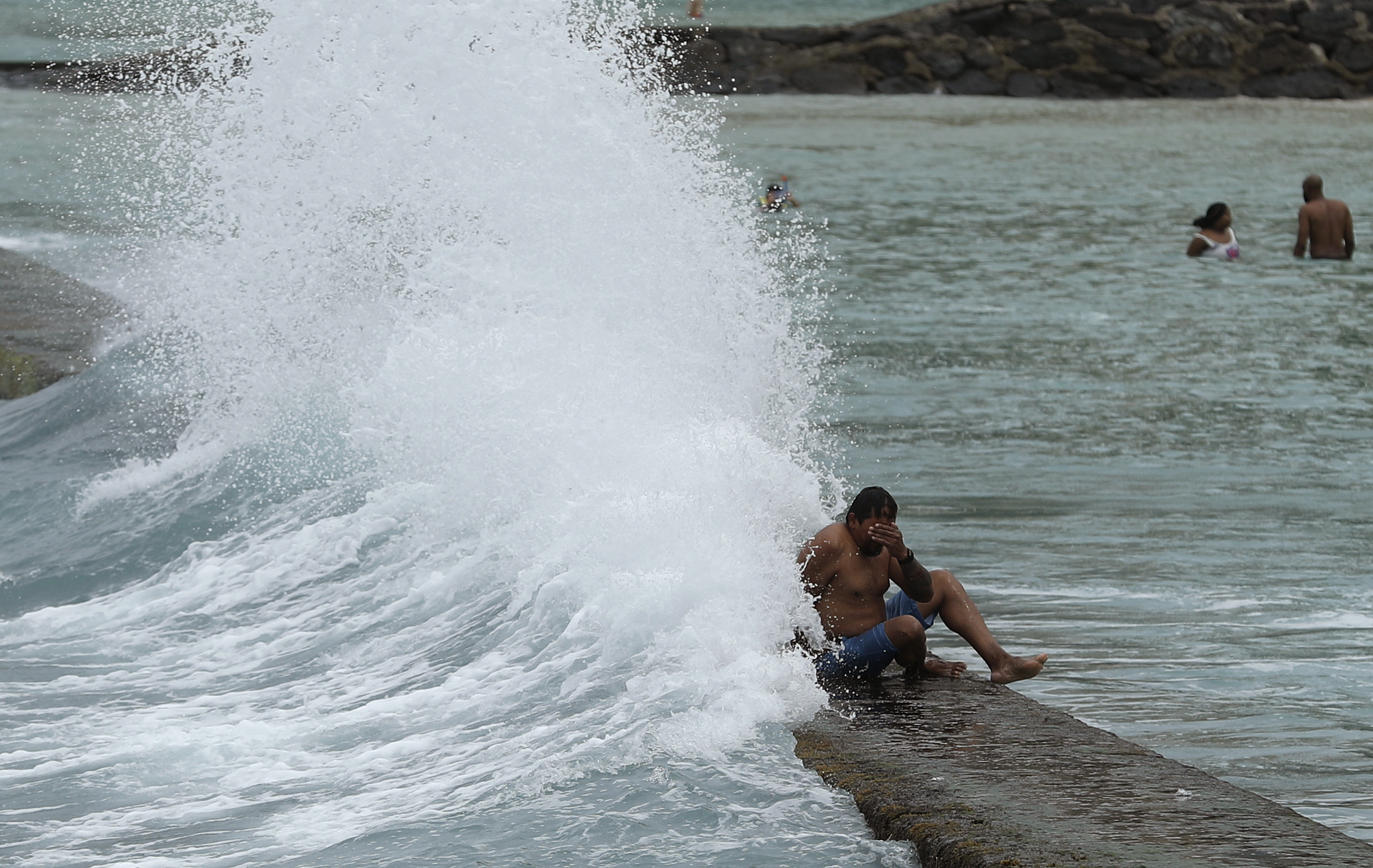 A large wave hits a man on a breakwater along Waikiki Beach ahead of Hurricane Lane, Friday, Aug. 24, 2018, in Honolulu.
