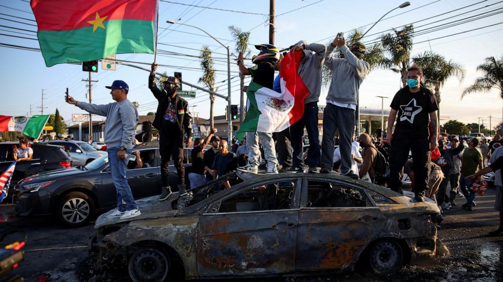 PHOTO: Protesters stand on a car destroyed during a standoff between police and protesters following multiple detentions by ICE, in the Los Angeles County city of Paramount, Calif., June 7, 2025.