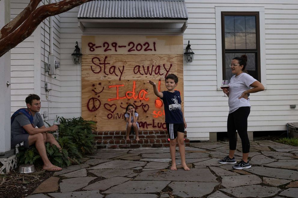 PHOTO: Jean-Luc Bourg, 8, catches a spider in front of his sister Olivia, 10, as his parents Jean Paul and Christina enjoy a glass of wine after boarding up their property in preparation for Hurricane Ida in Morgan City, La., Aug. 28, 2021.