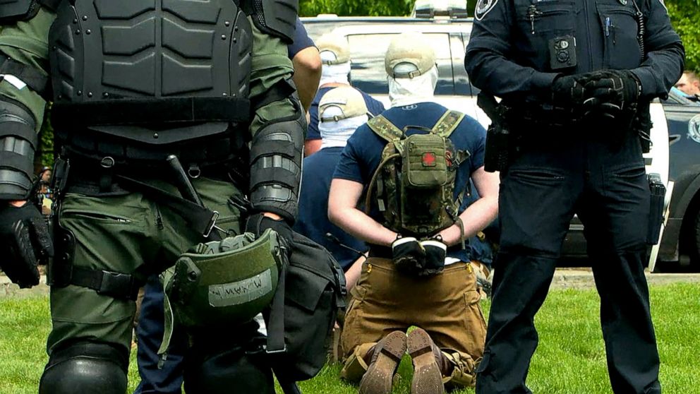 Police officers in riot gear guard a group of men, who police say are among 31 arrested for conspiracy to riot and are affiliated with the group Patriot Front, after they were found in the rear of a U Haul van in the vicinity of a Pride event in Idaho.