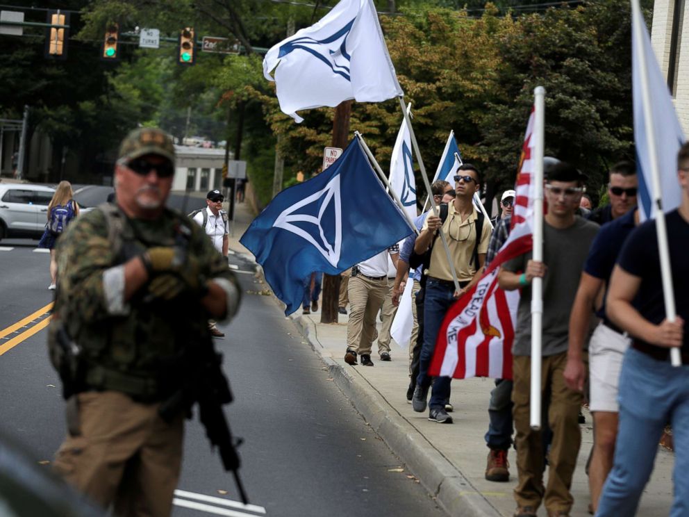 PHOTO: White nationalists carrying Identity Evropa flags pass a militia member as the they arrive for a rally in Charlottesville, Va., Aug. 12, 2017.