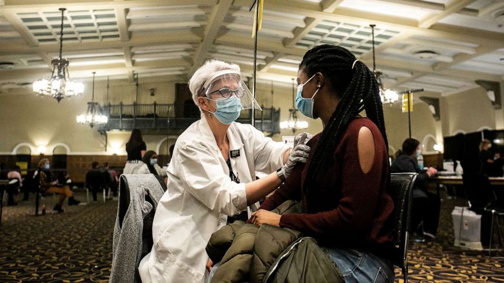 PHOTO: University of Iowa graduate student Precious Cummings, right, receives her first dose of the Pfizer-BioNTech COVID-19 vaccine from volunteer Paula Forest during a vaccination clinic, April 21, 2021, at the Iowa Memorial Union in Iowa City, Iowa.