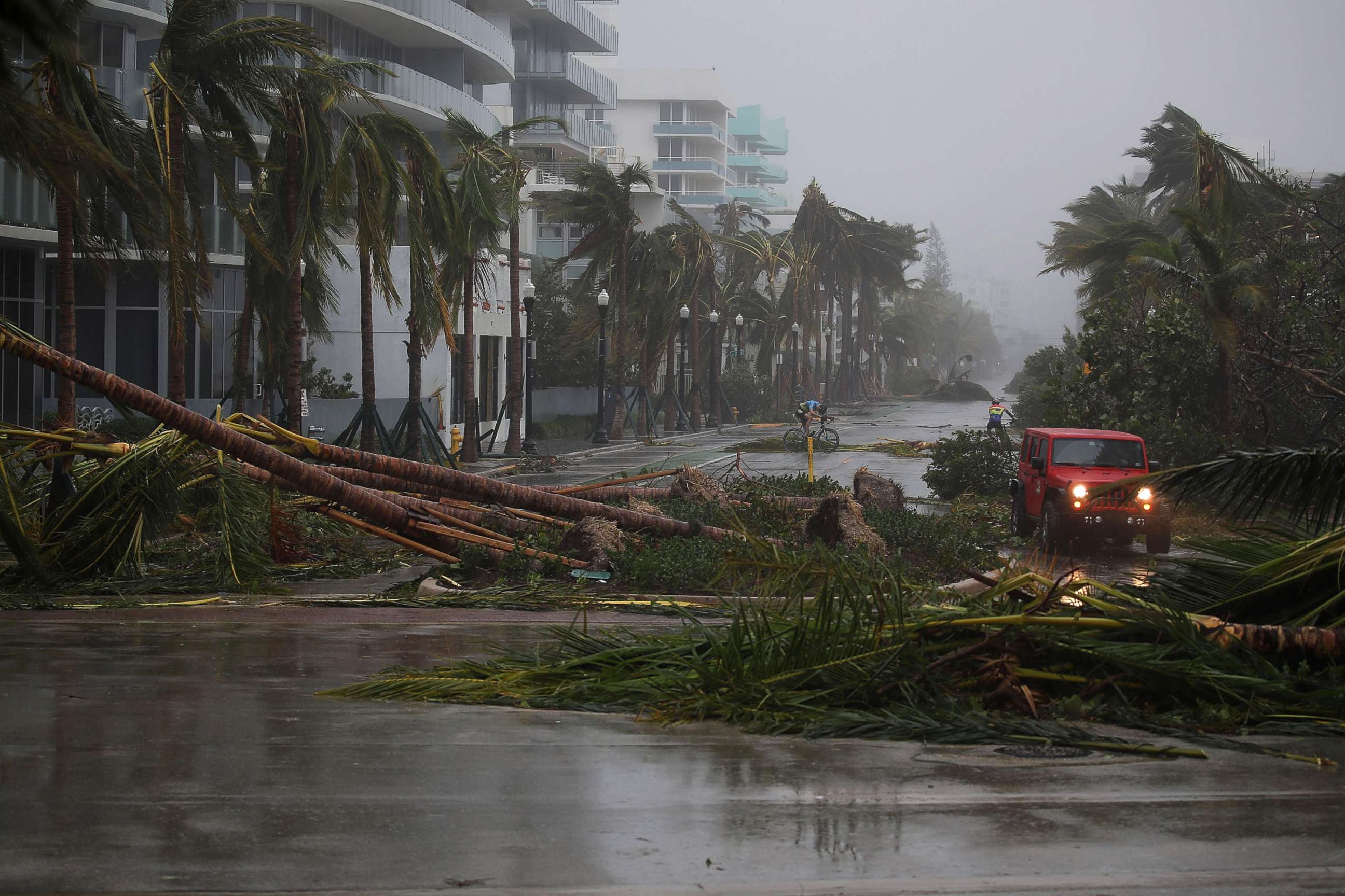 PHOTO: A vehicle passes downed palm trees and two cyclists attempt to ride as Hurricane Irma passes through the area on Sept. 10, 2017 in Miami Beach, Fla.