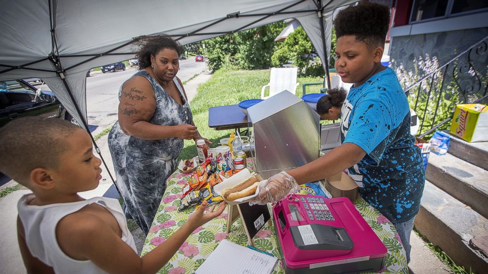 Thirteen-year-old hot dog entrepreneur Jaequan Faulkner serves up hot dogs to Yvonne Ross and her son Drameris Ross, 7, at his hot dog stand, July 16, 2018 in Minneapolis, Minn.