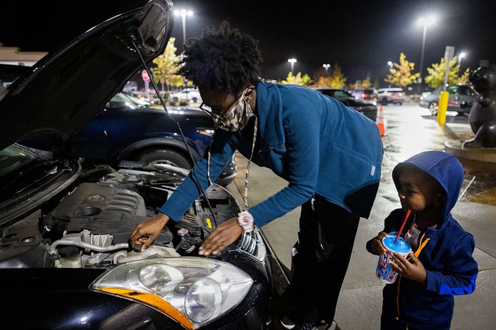 PHOTO: Jane Johnson, 29, adds coolant to her car while her son, watches while working for the delivery app, DoorDash, Oct. 29, 2021, in Birmingham, Ala.