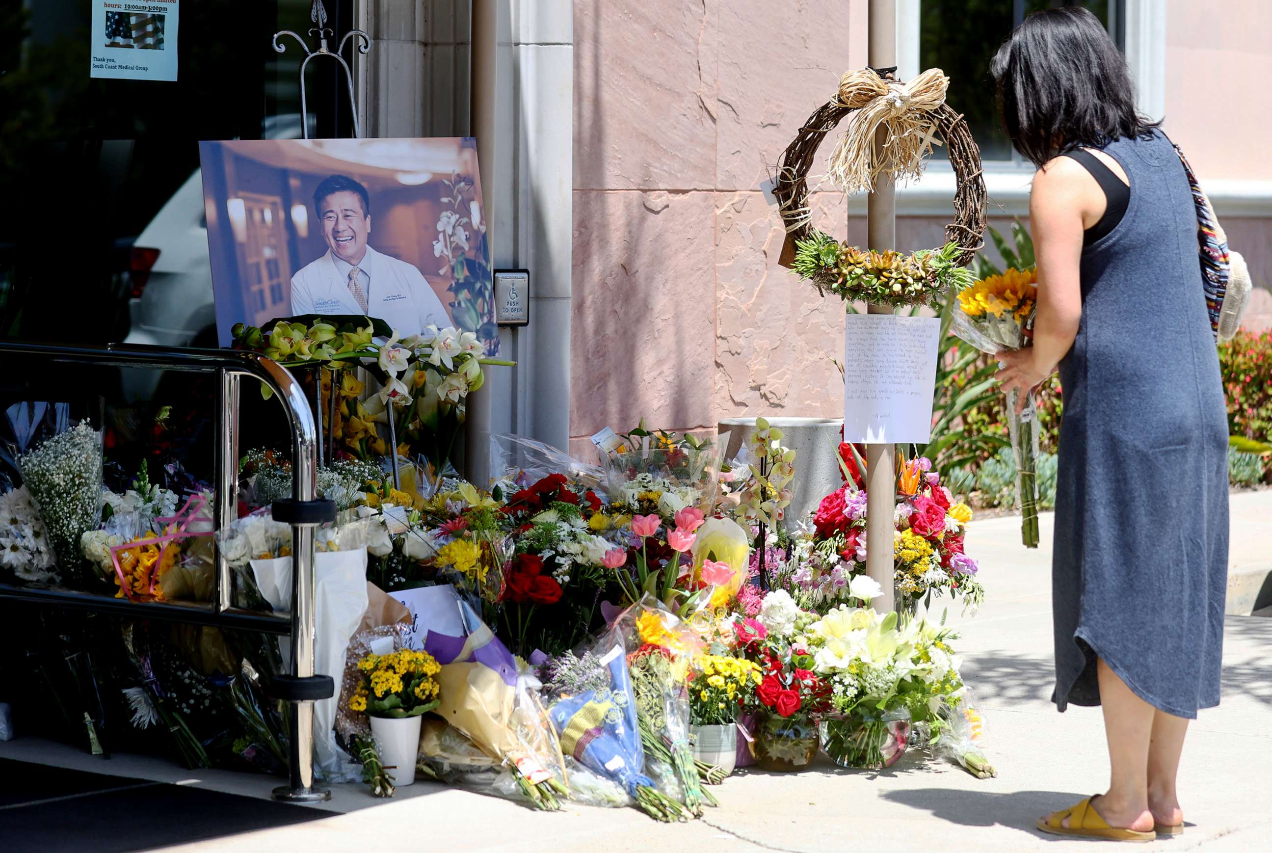 PHOTO: In this May 18, 2022, file photo, a person stands with flowers at a makeshift memorial for Dr. John Cheng outside his office in Aliso Viejo, Calif.