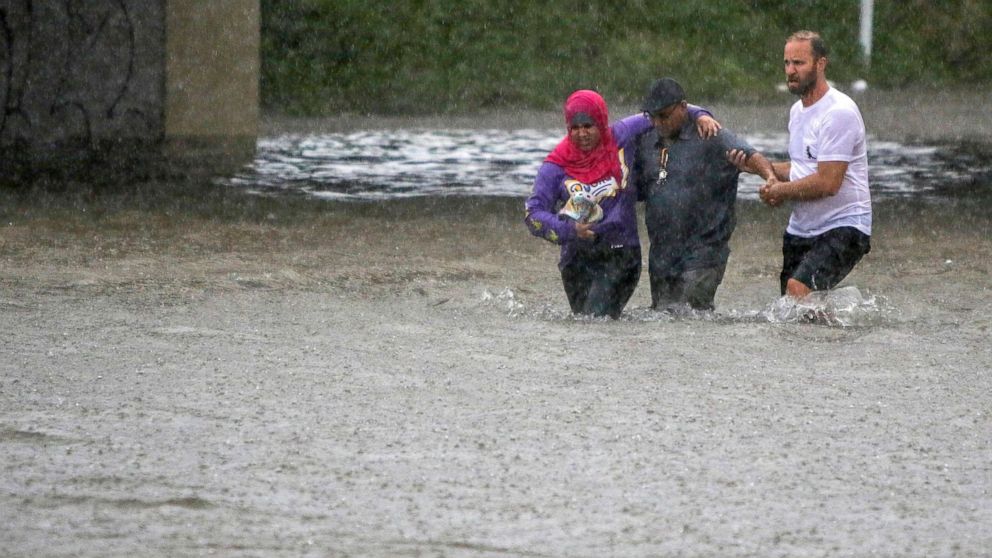 PHOTO: A man helps two people walk through flood water after their car got stuck in St. Louis, Mo., July 28, 2022.