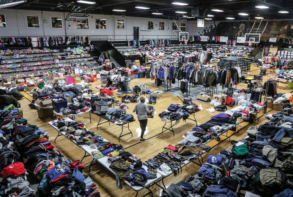 PHOTO: Volunteer Peggie Stewart carries a container of clothing amidst an expanse of donated items for those in need of tornado disaster relief in the main hall of the Central City Convention Center, on Dec. 16, 2021, in Central City, Ky.