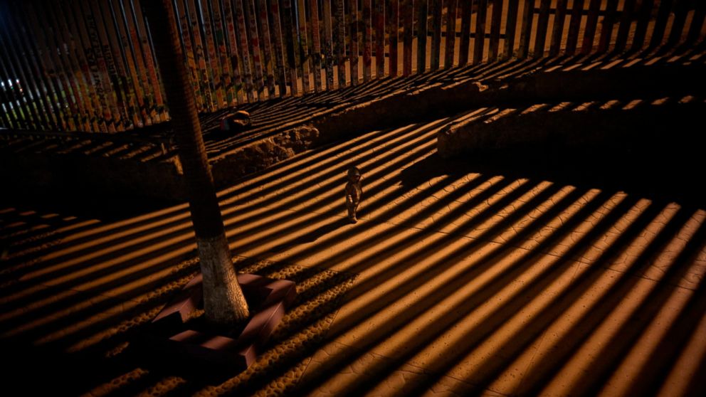 In this Jan. 11, 2019 photo, a boy plays as floodlights from the United States filter through the border wall in Tijuana, Mexico.