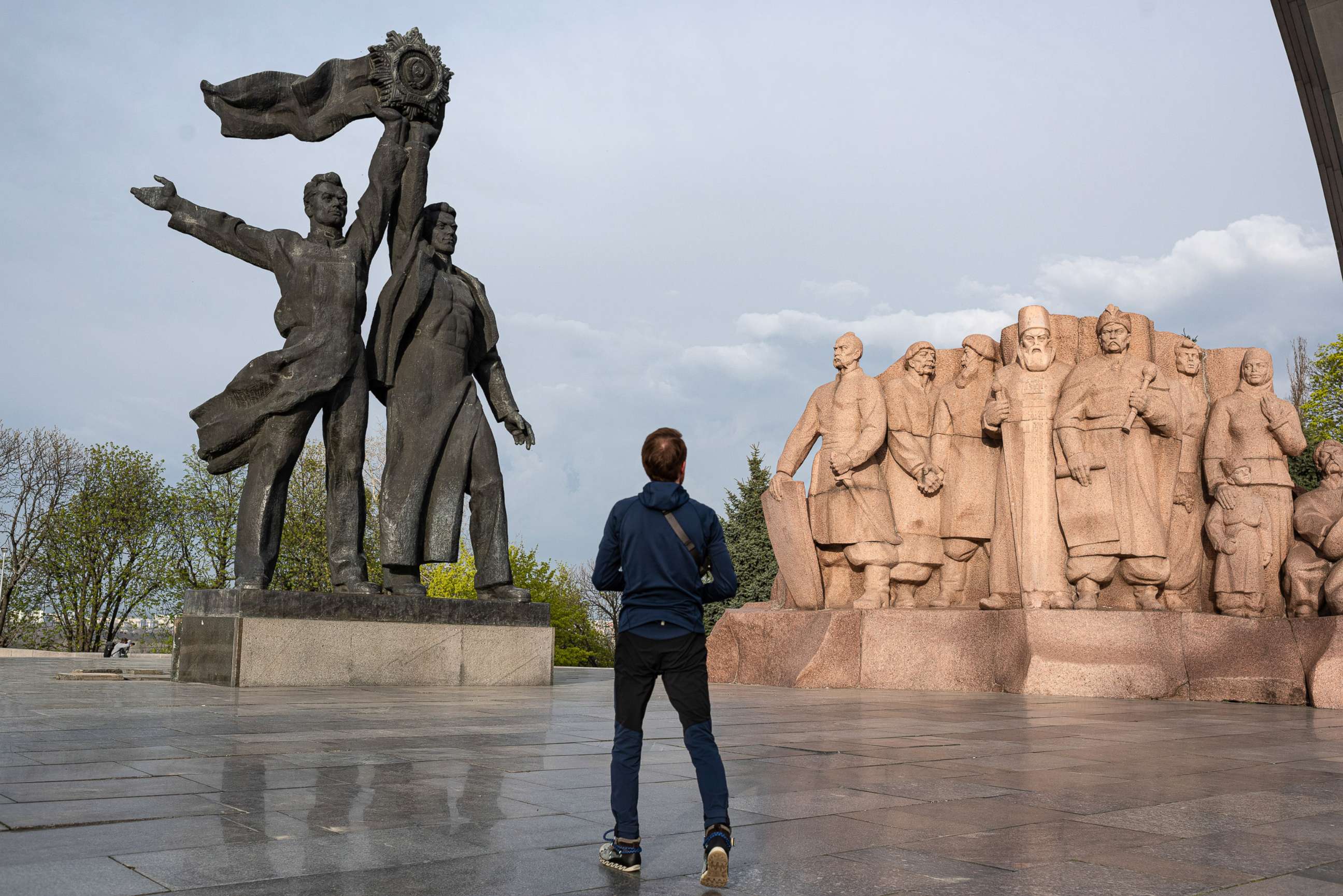 PHOTO: A man passes by the 'Friendship of Peoples' monument, left, and the monument dedicated to Pereiaslav agreement, right, April 25, 2022, in Kyiv, Ukraine.