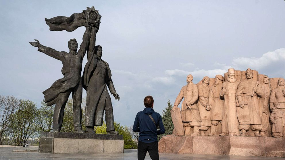 PHOTO: A man passes by the 'Friendship of Peoples' monument, left, and the monument dedicated to Pereiaslav agreement, right, April 25, 2022, in Kyiv, Ukraine.