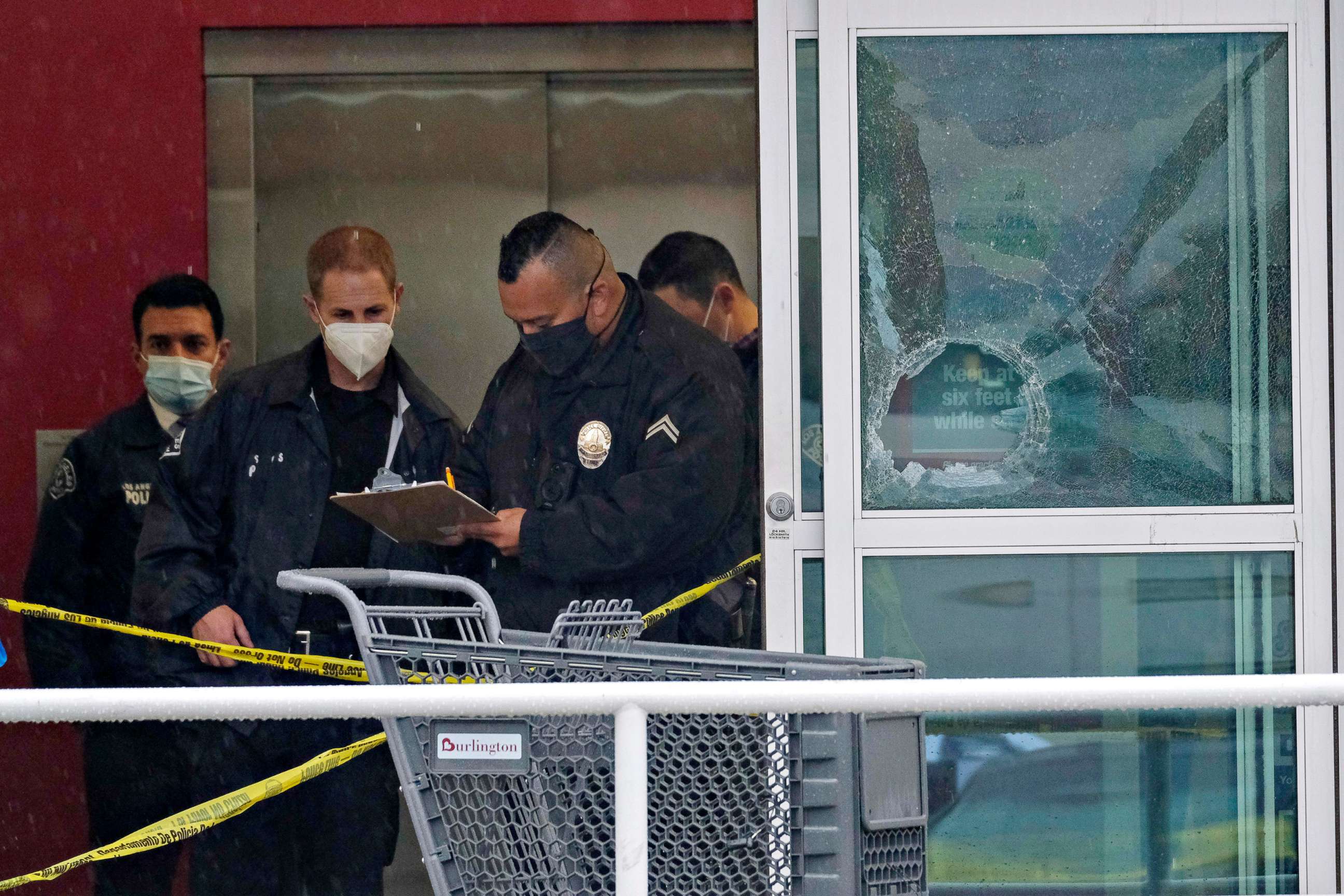 PHOTO: Police officers work near a broken glass door at the scene where two people were struck by gunfire, one of whom died, in a shooting at the Burlington coat factory store in North Hollywood, Calif., Dec. 23, 2021.