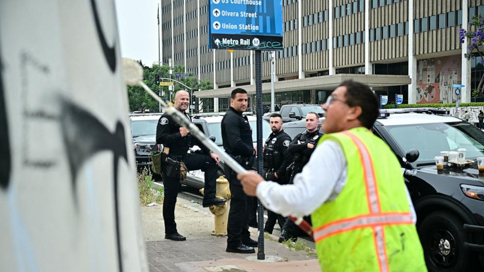 PHOTO: Police officers look on as a worker cleans a wall in Fletcher Bowron Square near the Edward Roybal Federal Building, following a night of protests in response to federal immigration operations in Los Angeles, June 9, 2025.