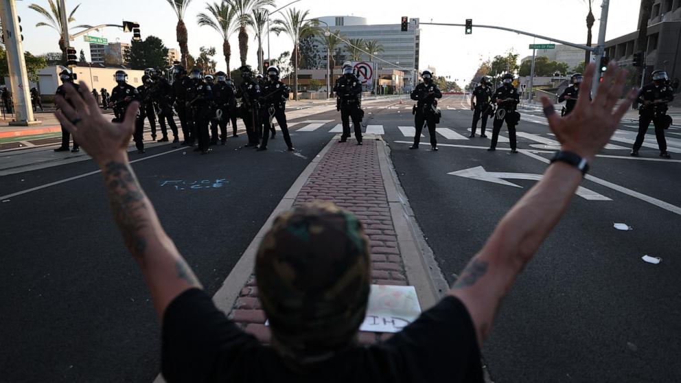 PHOTO: A person raises their hands facing a row of police outside the United States Citizenship and Immigration Services Santa Ana Field Office after reports of ICE raids in Santa Ana, Calif., June 9, 2025.