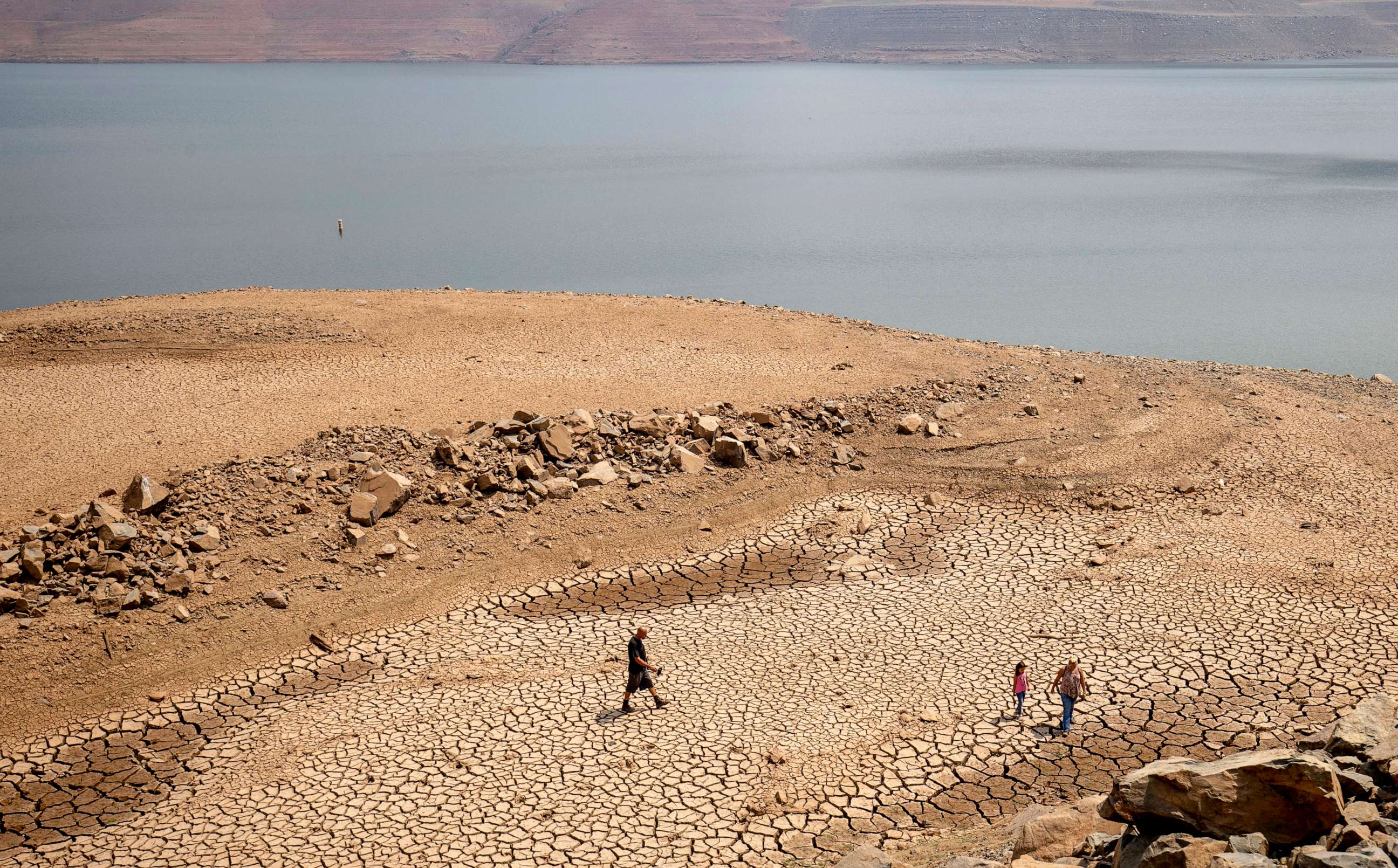 PHOTO: A family walks over cracked mud near Lake Oroville's shore as water levels remain low due to continuing drought conditions, Aug. 22, 2021, in Oroville, Calif.