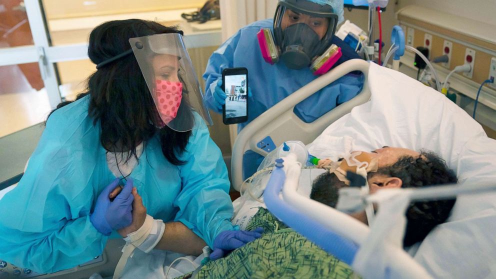 PHOTO: Patty Trejo looks at her intubated husband, Joseph, in a COVID-19 unit as registered nurse Celina Mande holds a smartphone showing a mariachi band performing for the patient outside of St. Jude Medical Center, in Fullerton, Calif., Feb. 15, 2021. 
