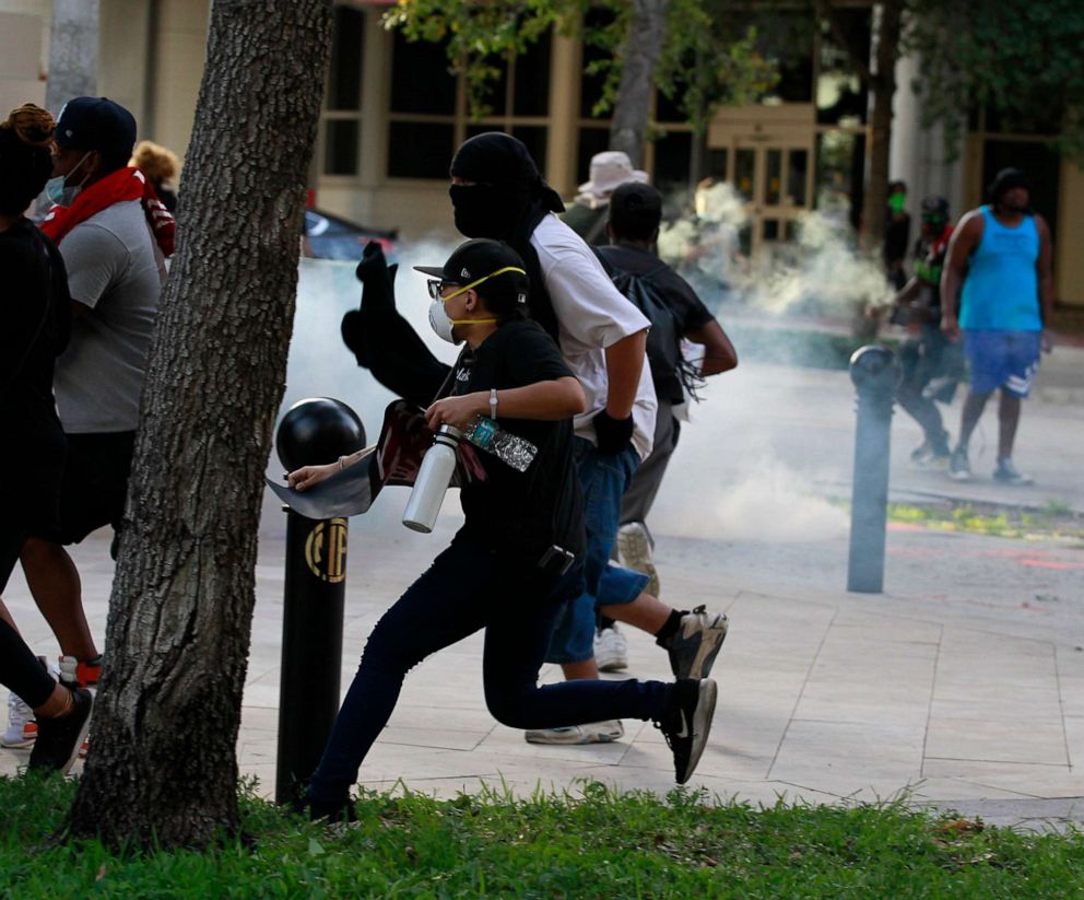 PHOTO: Protesters scatter as Fort Lauderdale police shoot tear gas at them near the  municipal garage in downtown Fort Lauderdale near Wayne Huizenga Park on May 31, 2020.