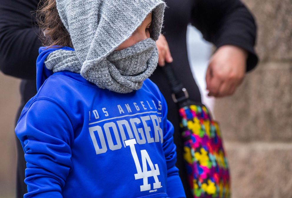 PHOTO: A little girl wears a scarf around her head as she lines up with her mother, looking to buy KN95 face masks outside Masataco, a taco shop in Whittier, Calif., Tuesday, April 7, 2020. 