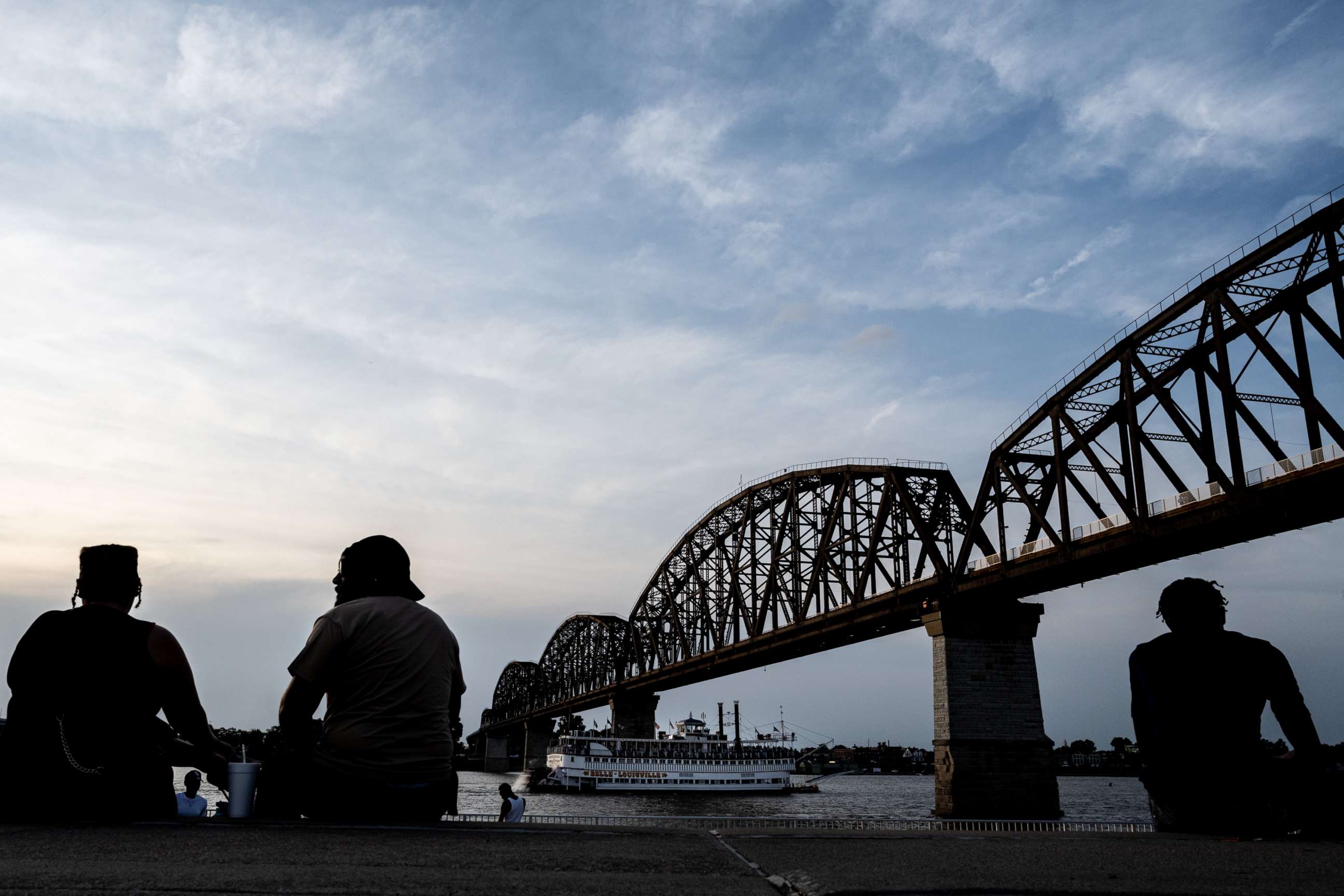 PHOTO: Silhouetted people sit near the river as the Belle of Louisville as a riverboat, passes under the Big Four Bridge in Louisville, Ky., June 19, 2021.