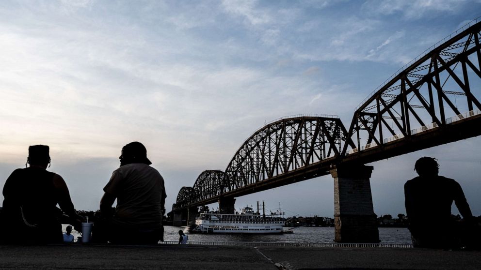 PHOTO: Silhouetted people sit near the river as the Belle of Louisville as a riverboat, passes under the Big Four Bridge in Louisville, Ky., June 19, 2021.