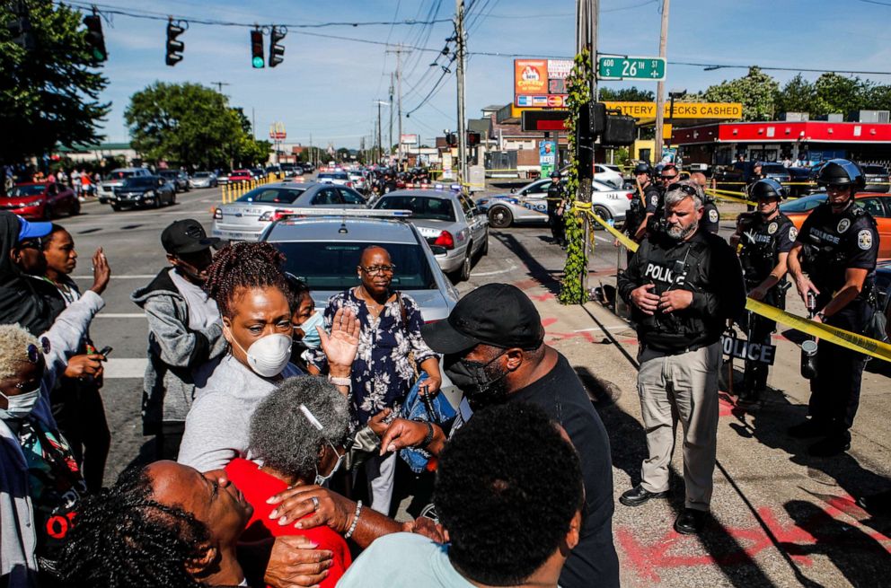 PHOTO: Odessa Riley, in red, is comforted by family as she is lead in prayer outside police tape as police watch outside Dino's Food Mart in the Russell neighborhood of Louisville, Ky., June 1, 2020.