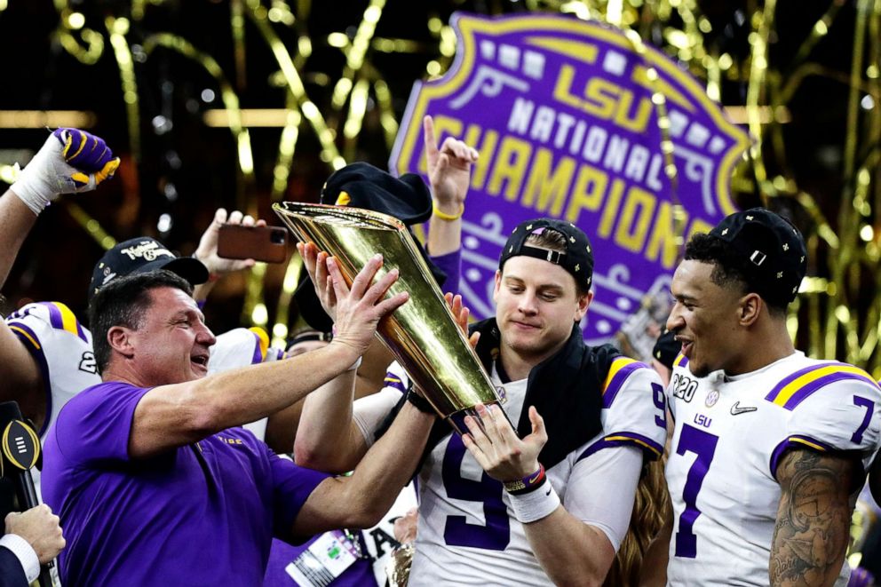 PHOTO: LSU head coach Ed Orgeron, left, and quarterback Joe Burrow, center, hold the trophy beside safety Grant Delpit after a NCAA College Football Playoff national championship game against Clemson, Jan. 13, 2020, in New Orleans. LSU won 42-25.