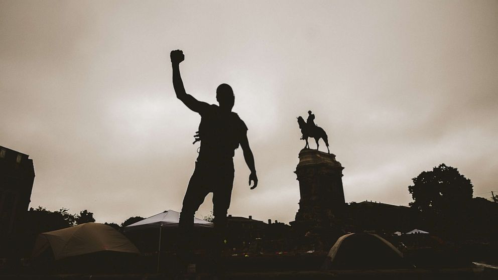 PHOTO: This photo taken on June 20, 2020, shows a silhouette of a man with his fist in the air at the Robert E. Lee monument in Richmond, Virginia. Protesters for racial justice have called for statues of Confederate leaders, like Lee, to be taken down.
