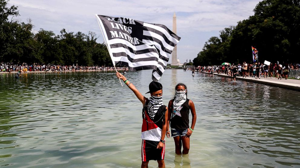PHOTO: A demonstrator holds a Black Lives Matter flag as he wades into the waters of the Lincoln Memorial reflecting pool as protesters gather in Washington, D.C., Aug. 28, 2020. 