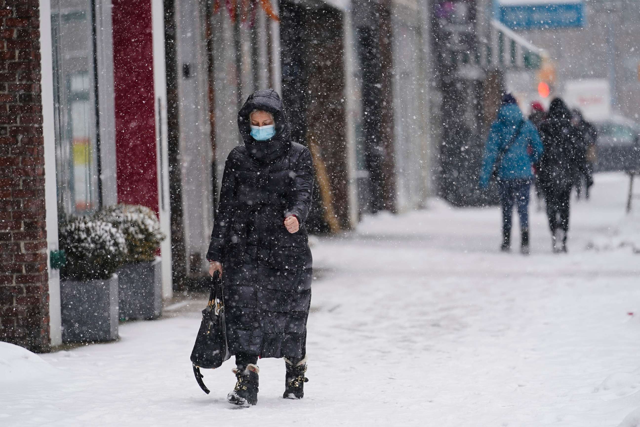 PHOTO: Pedestrians wear protective masks during the coronavirus pandemic as they walk along 71st Avenue as snow falls, Feb. 18, 2021, in the Queens borough of New York. 