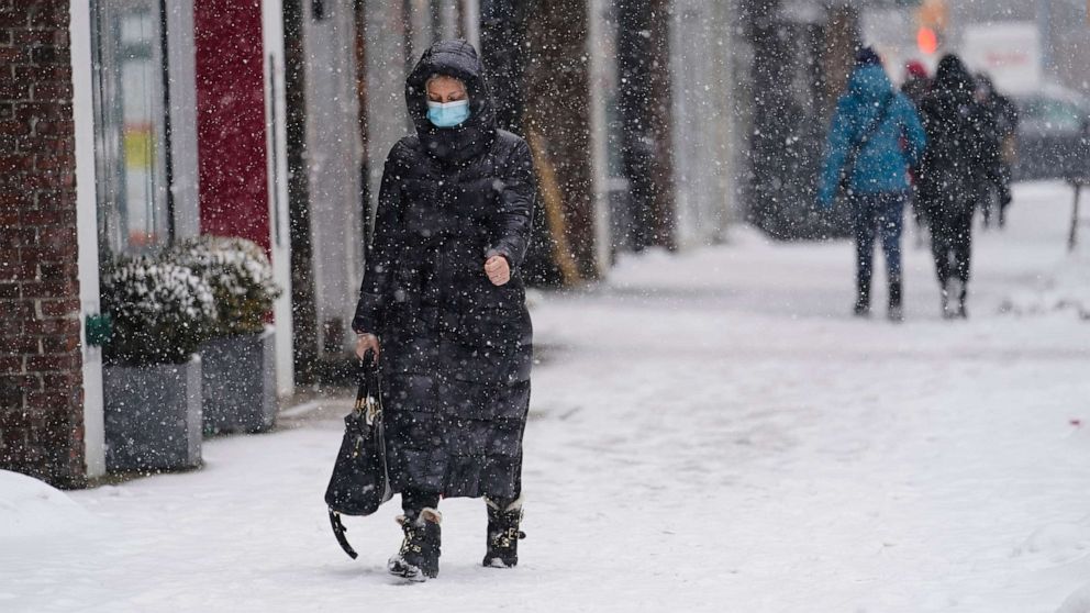 PHOTO: Pedestrians wear protective masks during the coronavirus pandemic as they walk along 71st Avenue as snow falls, Feb. 18, 2021, in the Queens borough of New York. 