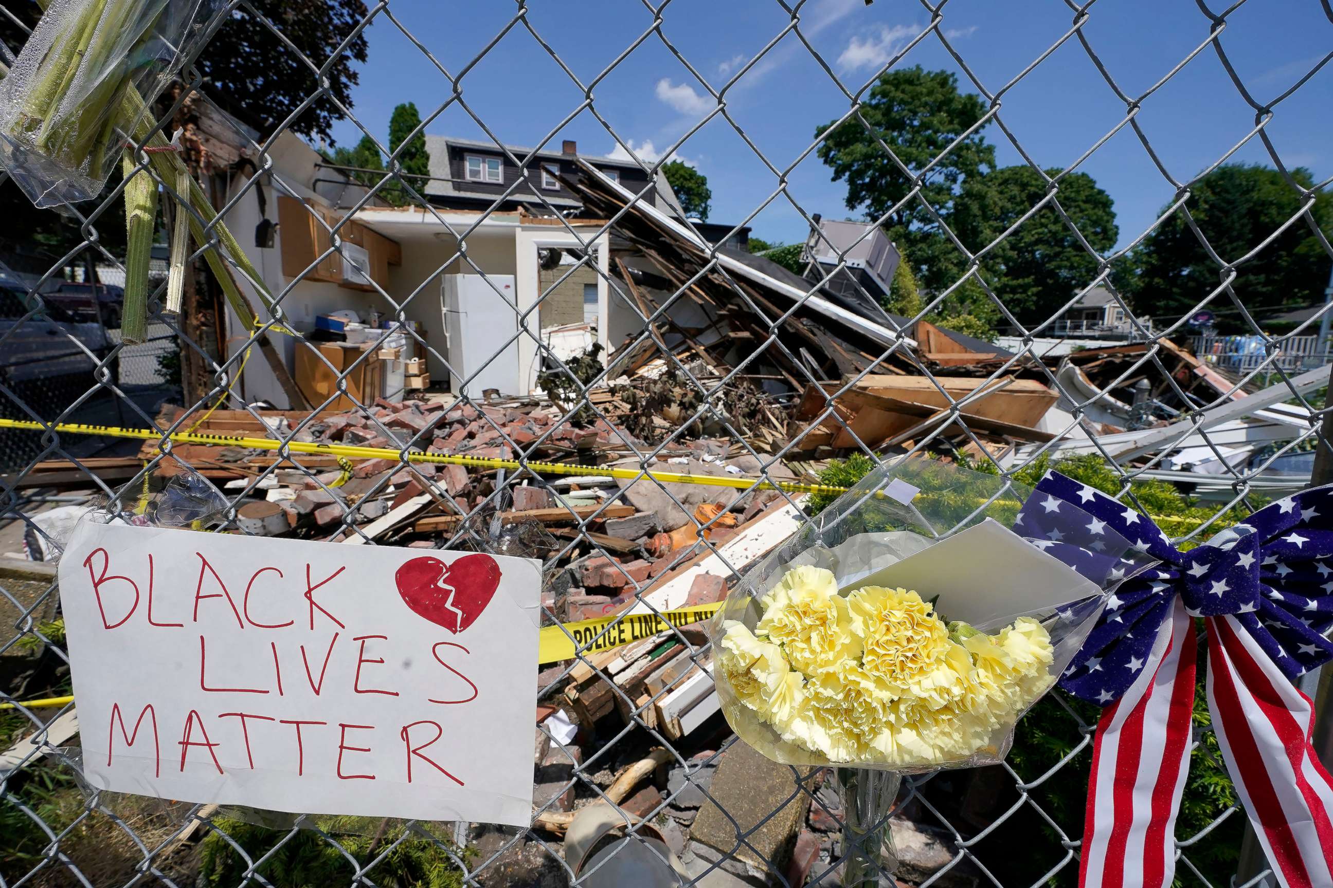 PHOTO: Signs and flowers are attached to a fence outside a building in Winthrop, Mass., June 28, 2021, where an armed man crashed a hijacked truck, on June 26, 2021, then fatally shot two people before being killed by police.