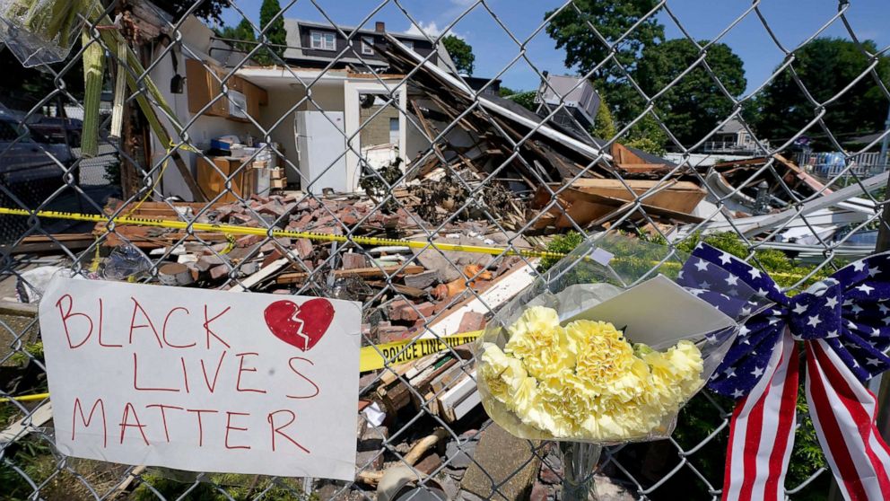 PHOTO: Signs and flowers are attached to a fence outside a building in Winthrop, Mass., June 28, 2021, where an armed man crashed a hijacked truck, on June 26, 2021, then fatally shot two people before being killed by police.