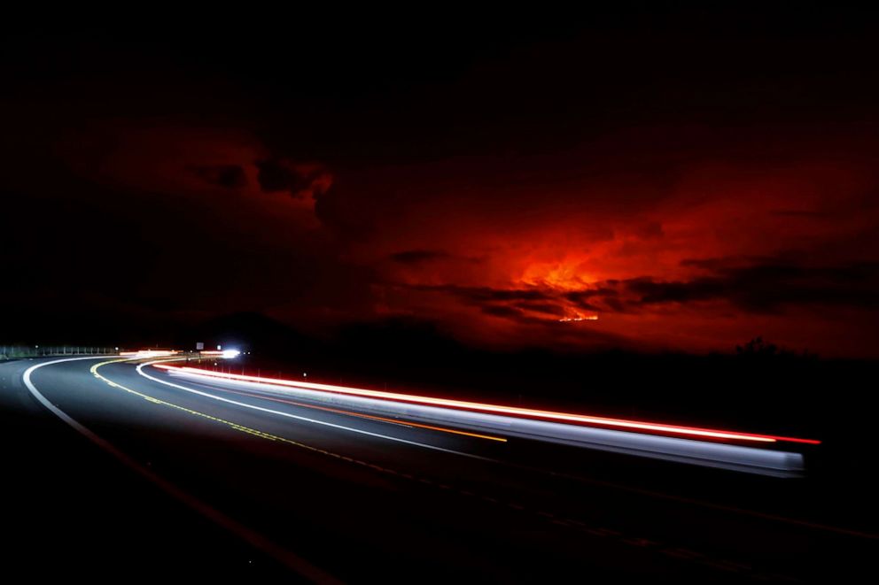 PHOTO: In this long camera exposure, cars drive down Saddle Road as Mauna Loa erupts in the distance, Nov. 28, 2022, near Hilo, Hawaii.