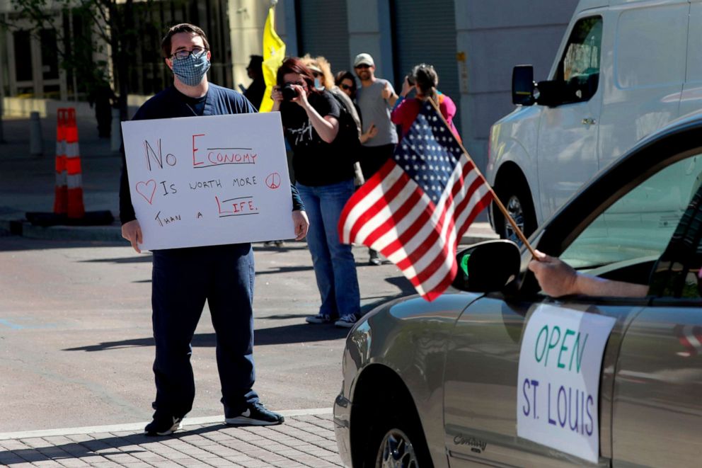 PHOTO: Alex Cummings, an ICU nurse at St. Louis University Hospital, stands in the middle of the street, blocking cars protesting the stay-at-home orders on April 21, 2020, in Clayton, Mo.